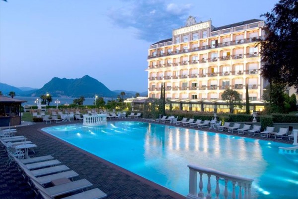 Osvetlený hotel pri vonkajšom bazéne s horami v pozadí.
