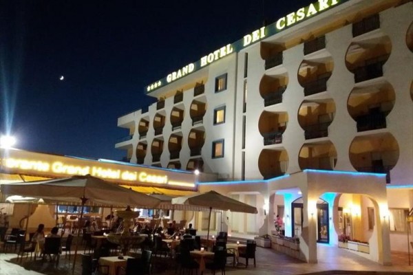 Večerný pohľad na osvetlený Grand Hotel dei Cesari s vonkajšou reštauráciou.