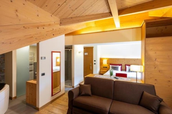Podkrovný apartmán s drevenými trámami, sedačkou a manželskou posteľou v pozadí.