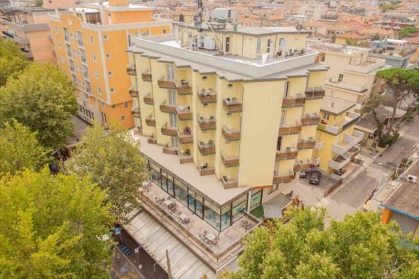 Výšková budova s balkónmi a terasou uprostred mestskej zástavby.