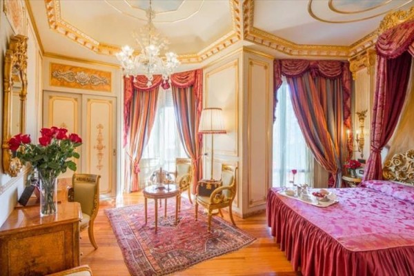 Luxusná izba s elegantným nábytkom, zlatými detailmi a červenými závesmi.  