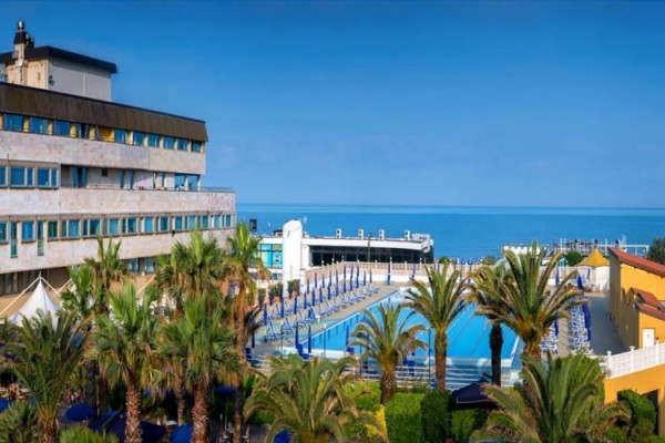 Hotel s bazénom obklopený palmami pri mori.