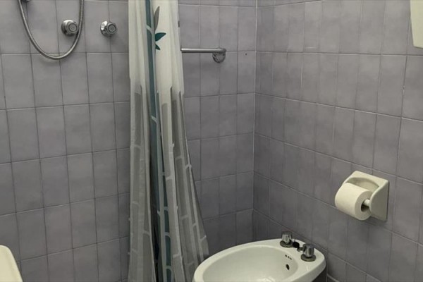 Kúpeľňa so sivými obkladmi, sprchovacím kútom, umývadlom, bidetom a toaletným papierom na stene.