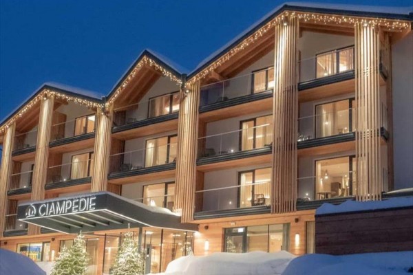 Moderný drevený horský hotel v zime s osvetlením a snehom na streche.