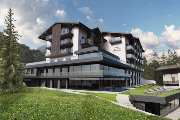 Moderný hotel obklopený horami a lesmi so sklenenými terasami a relaxačnými lehátkami na zelenej tráve.