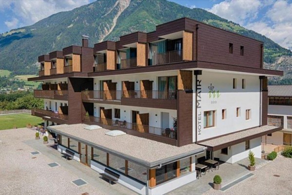 Moderný hotel s drevenými balkónmi pred horskou panorámou.