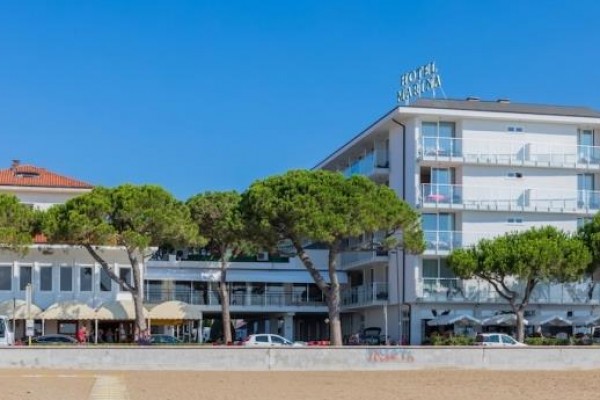 Moderný hotel s balkónmi a zelenými stromami v popredí.