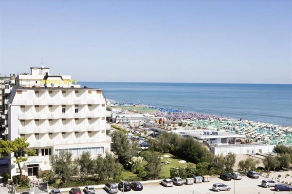 Výhľad na hotel vedľa pláže s modrými a zelenými slnečníkmi pri mori.