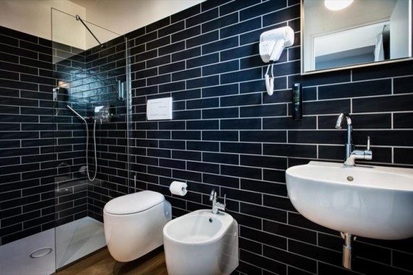 Moderná kúpeľňa s tmavými obkladmi obsahujúca sprchový kút, toaletu, bidet a umývadlo.