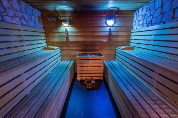 Drevená sauna s lavičkami, pecou a modrým osvetlením.  