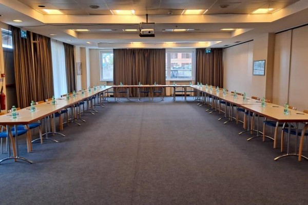 Konferenčná miestnosť s usporiadaním stolov do tvaru U a fľašami vody na každom stole.  