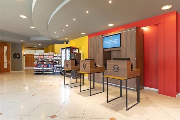 Hotelová recepcia so samoobslužnými kioskami a regálmi s tovarom.