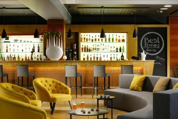 Elegantný hotelový bar s modernými sedacími súpravami a výberom alkoholických nápojov na policiach.