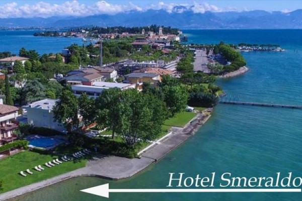 Pohľad na pobrežie so zeleňou a budovami pri jazere s označením Hotel Smeraldo.