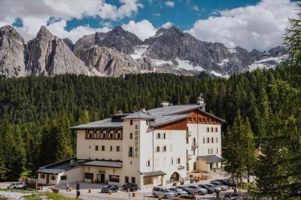 Hotel obklopený lesom s horským masívom v pozadí.