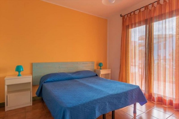 Izba s modrou posteľou, žltou stenou a oranžovými závesmi pri veľkom okne.