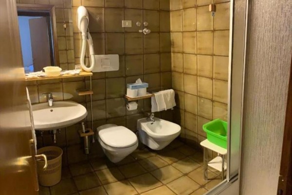Kúpeľňa s umývadlom, toaletou, bidetom a sprchovacím kútom, hnedé dlaždice na stenách.