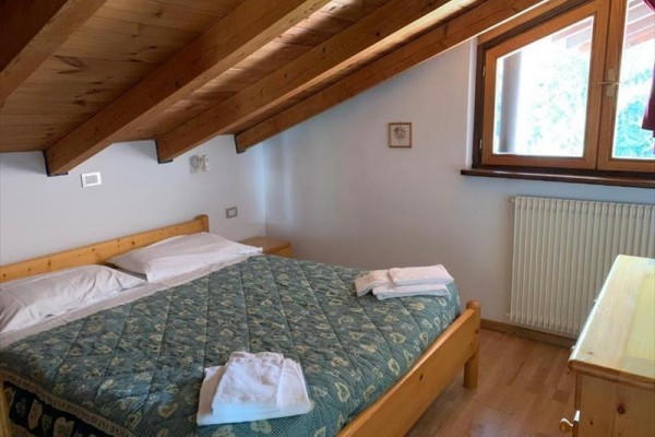 Podkrovná spálňa s drevenou posteľou a oknom.