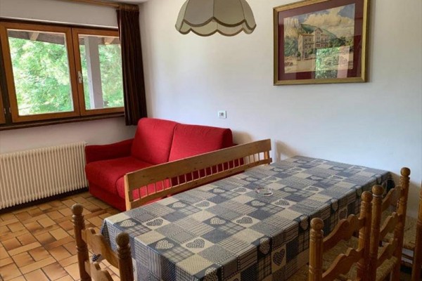 Izba s červenou pohovkou, dreveným stolom a stoličkami, s oknom a závesmi.