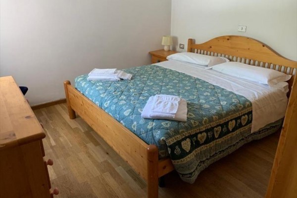 Spálňa s drevenou manželskou posteľou, modrozelenou prikrývkou a zloženými uterákmi.