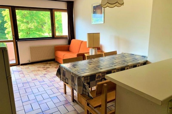 Slnečná obývacia izba s oranžovou pohovkou, jedálenským stolom a veľkými oknami s výhľadom na zeleň.