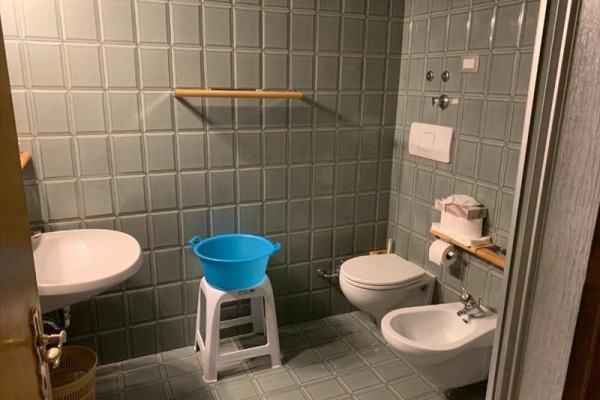 Kúpeľňa s umývadlom, toaletou, bidetom a modrým plastovým vedrom na stoličke.