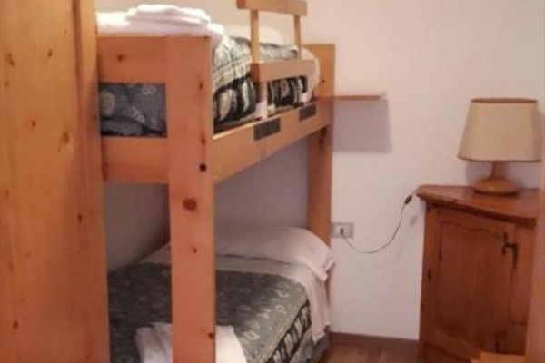 Poschodová posteľ s dreveným rámom vedľa stolíka s lampou.