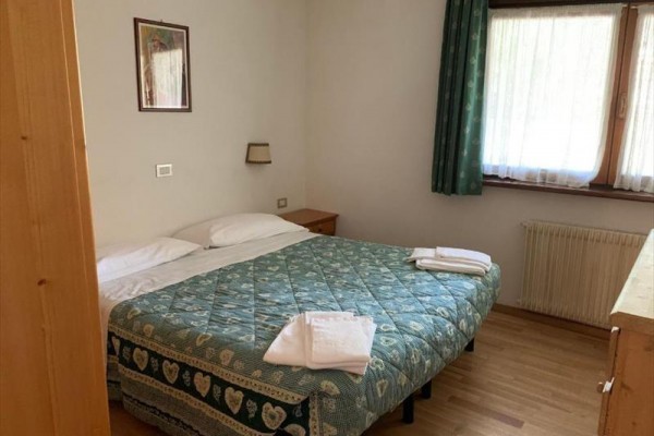 Spálňa s manželskou posteľou, zelenou prikrývkou, nočným stolíkom a oknom so závesom.