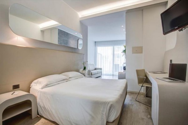 Moderná hotelová izba s manželskou posteľou, pracovným stolom a balkónom.