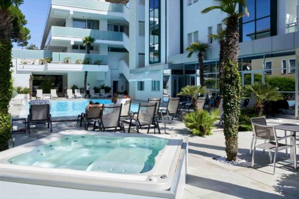 Moderný hotel s bazénom, vírivkou a vonkajším posedením obklopený palmami.