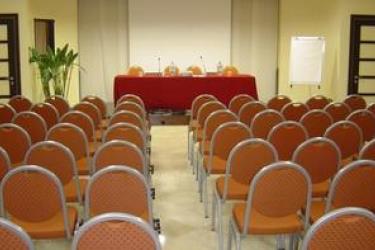 Konferenčná miestnosť s radami prázdnych stoličiek a stolom s mikrofónmi.