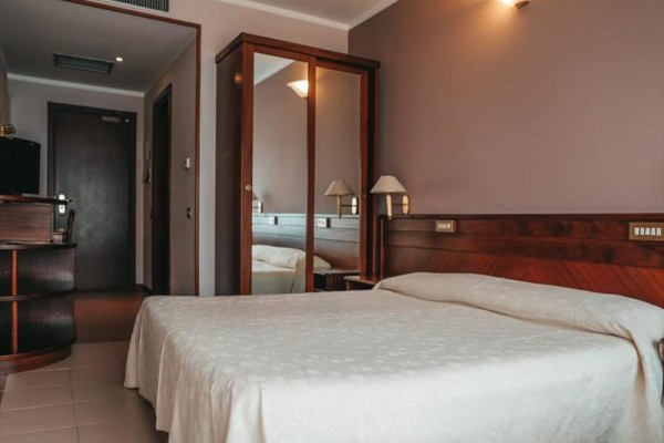 Hotelová izba s manželskou posteľou a zrkadlovou skriňou.