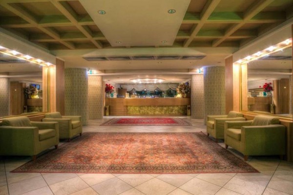 Hotelová lobby s kobercami, kreslami a recepciou v pozadí.