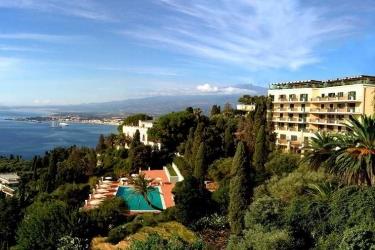 Hotel s bazénom obklopený stromami s výhľadom na pobrežie a more.