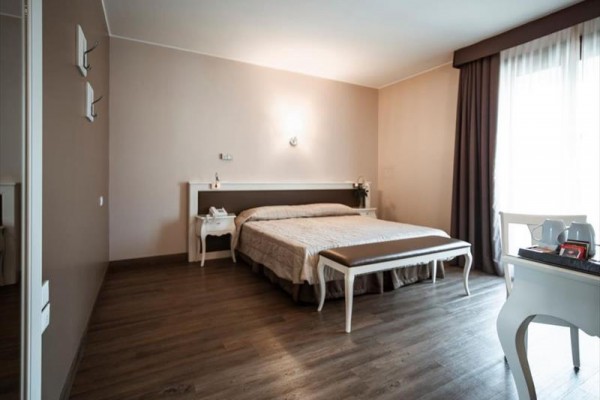 Moderná hotelová izba s manželskou posteľou, nočnými stolíkmi a písacím stolom.