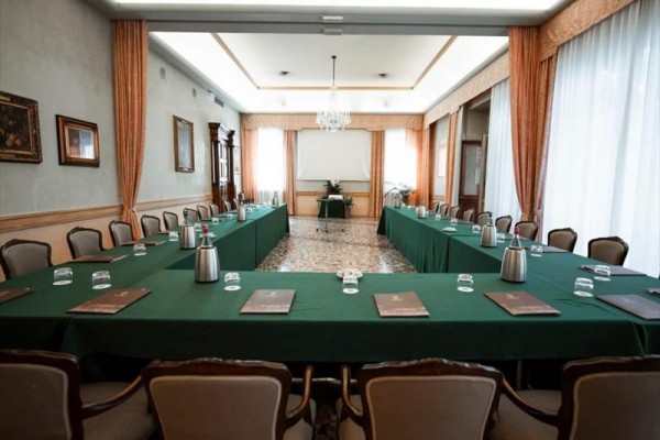 Konferenčná miestnosť s usporiadaním do tvaru U, zelenými obrusmi a stoličkami okolo stolov.