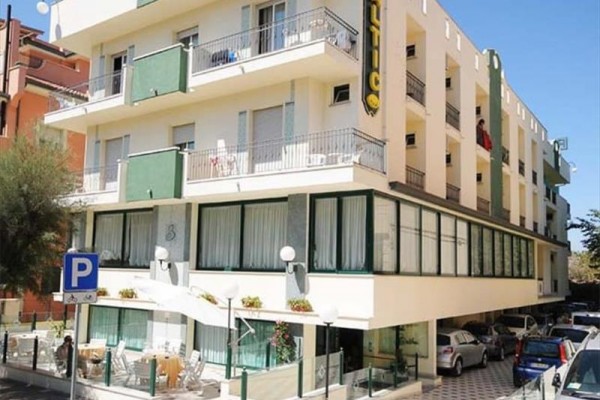 Plážový hotel so štyrmi poschodiami a parkoviskom na rohu ulice.