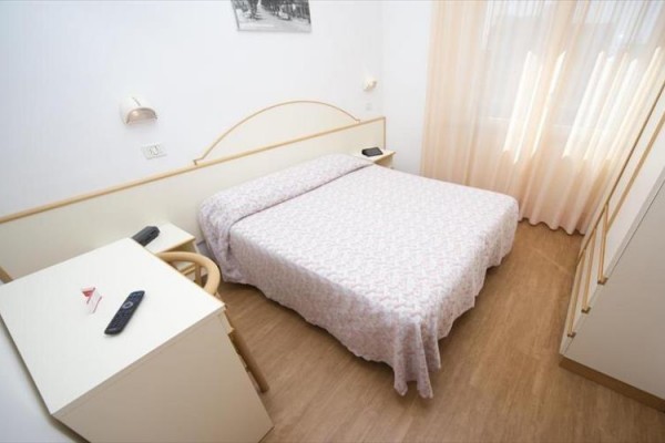 Svetlá izba s manželskou posteľou, stolom a stoličkami.