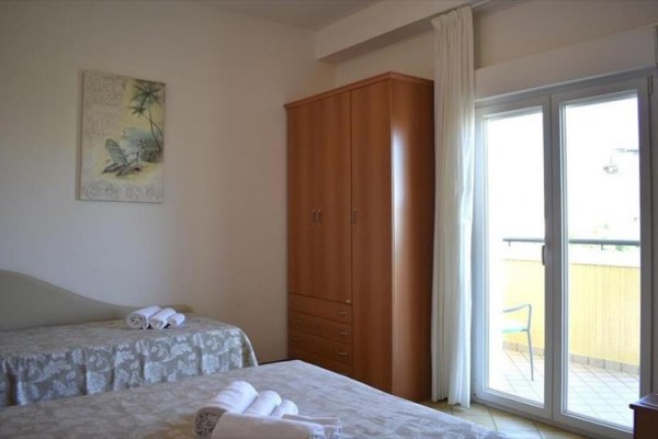 Spálňa s dvoma posteľami, skriňou a otvorenými dverami na balkón.