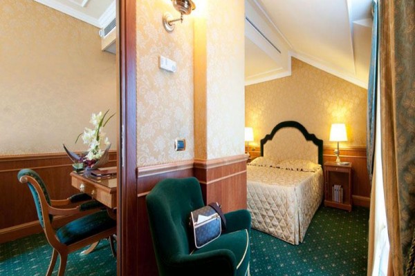 Elegantná hotelová izba s manželskou posteľou a pracovným stolom.