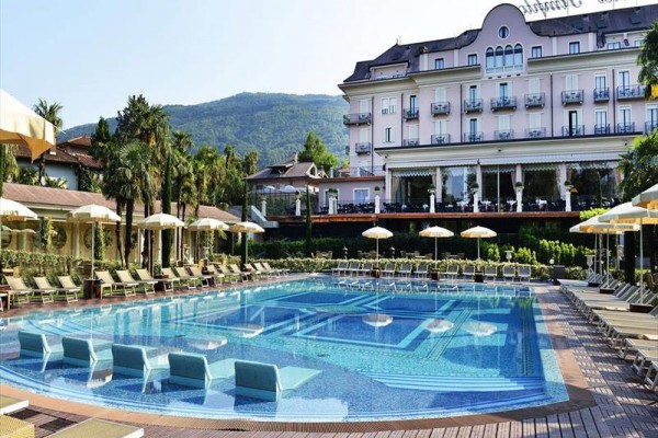 Hotel s vonkajším bazénom a lehátkami, v pozadí zelené hory.