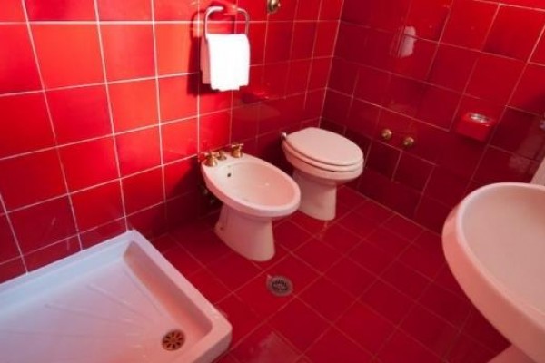 Kúpeľňa s červenými kachličkami, obsahujúca sprchu, bidet, toaletu a umývadlo.