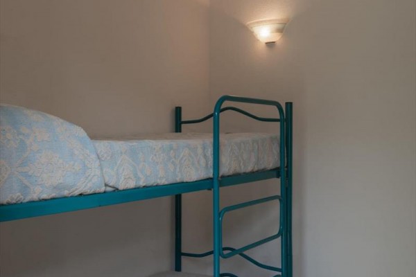 Kovová poschodová posteľ s modrými matracami pri bielej stene so svetlom.