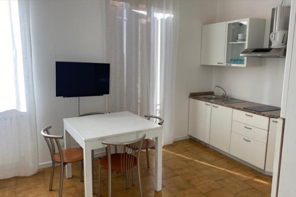 Svetlá kuchyňa s bielym nábytkom, stolom a televízorom na stene.