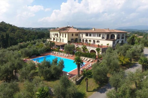 Hotel s bazénom obklopený olivovníkmi a zeleňou v vidieckej krajine.