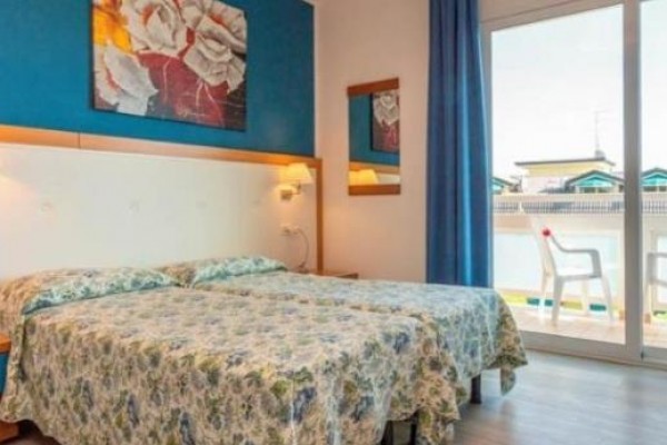 Dvojlôžková izba s modrou stenou, obrazom a balkónom s plastovými stoličkami.