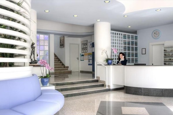 Moderná recepcia s bielym pultom, modrou pohovkou a kvetináčom s orchideami.