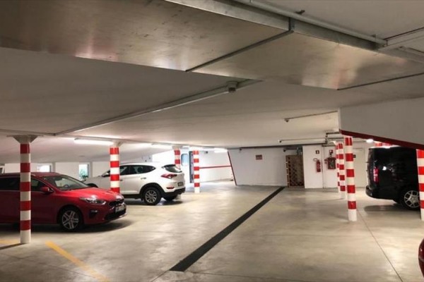 Podzemné parkovisko s niekoľkými zaparkovanými autami a stĺpmi s červenobielymi pruhmi.