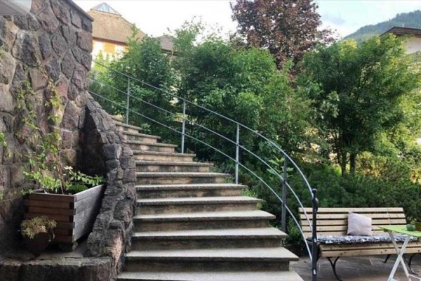Vonkajšie kamenné schody s kovovým zábradlím vedľa lavičky a zelene.