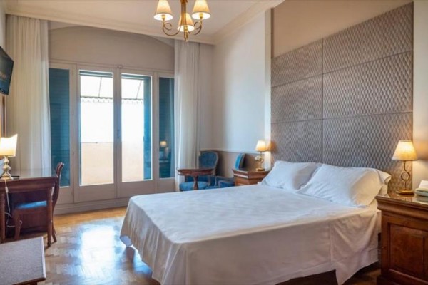Elegantná hotelová izba s manželskou posteľou, písacím stolom a francúzskym oknom.